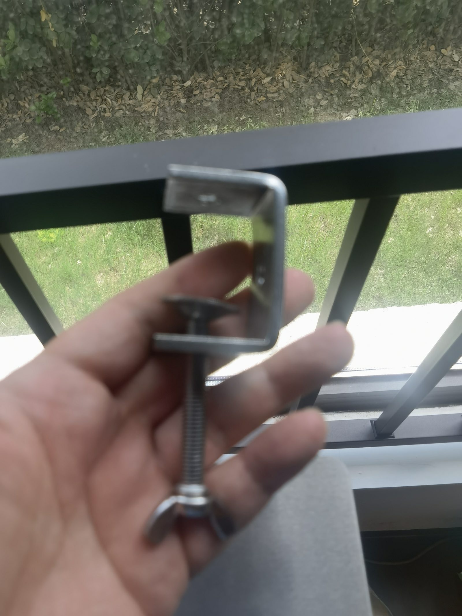 A abraçadeira em C ajustável — apertada na mão, sem ferramenta.